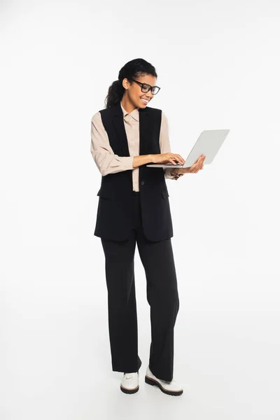 Comprimento total de sorridente mulher de negócios afro-americana usando laptop no fundo branco — Fotografia de Stock
