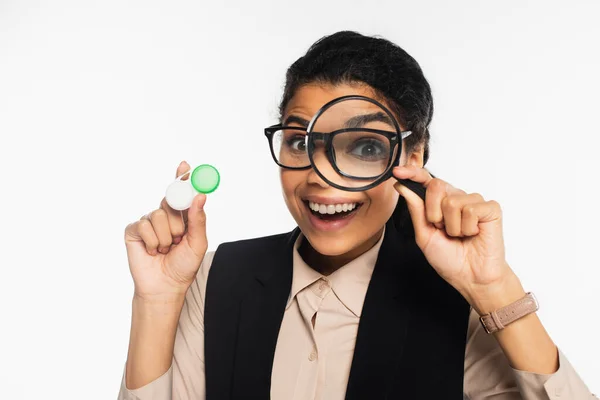 Smiling african american businesswoman in eyeglasses holding contact lenses and magnifying glass isolated on white — Stock Photo