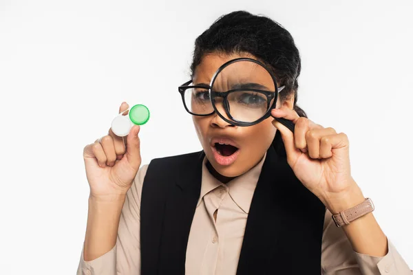 Shocked african american businesswoman holding magnifying glass and contact lenses isolated on white — Stock Photo