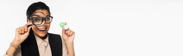 Cheerful african american businesswoman holding magnifying glass and contact lenses isolated on white, banner — Stock Photo