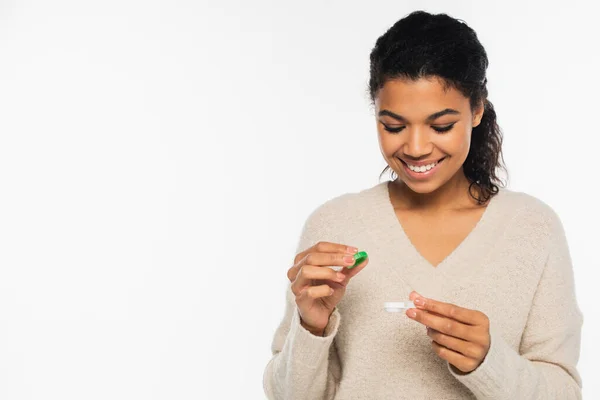 Lächelnde Afroamerikanerin hält Container mit Kontaktlinsen isoliert auf weiß — Stockfoto
