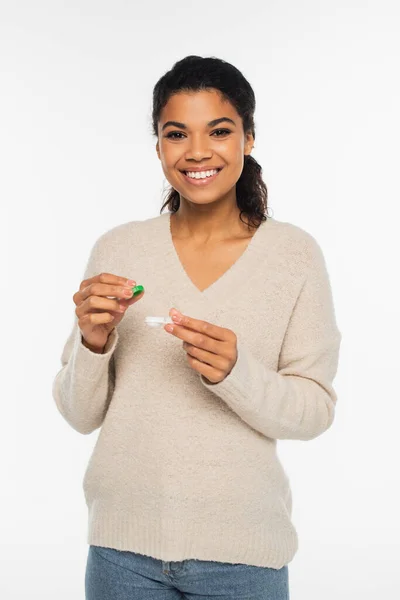Cheerful african american woman in sweater holding contact lenses isolated on white — Stock Photo