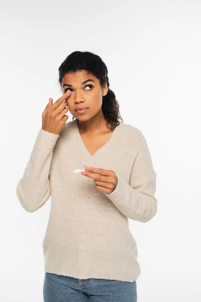 Young african american woman in sweater wearing contact lens isolated on white — Stock Photo