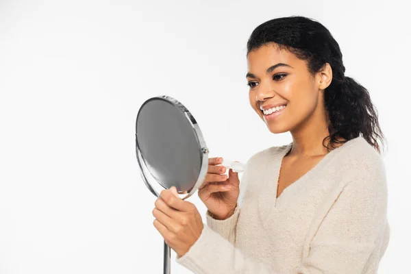 Smiling african american woman holding mirror and contact lenses isolated on white — Stock Photo
