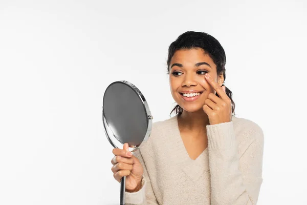 Mulher afro-americana positiva vestindo lente de contato e segurando espelho isolado no branco — Fotografia de Stock