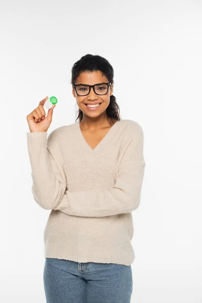 Smiling african american woman in eyeglasses holding container with contact lenses isolated on white — Stock Photo