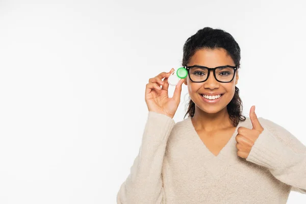 Femme afro-américaine souriante aux lunettes tenant des lentilles de contact et montrant un geste similaire isolé sur du blanc — Photo de stock