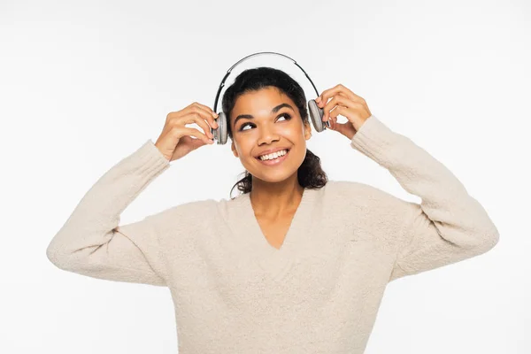 Mulher americana africana alegre em suéter segurando fones de ouvido isolados em branco — Fotografia de Stock