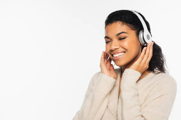 Позитивна афро-американська жінка в светрі прослуховує музику в навушниках ізольованих на білому — стокове фото