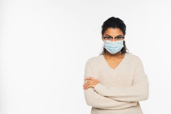 Mujer afroamericana en gafas y máscara médica de pie con brazos cruzados aislados en blanco - foto de stock