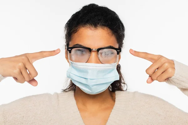 Femme afro-américaine en masque médical pointant vers des lunettes brumeuses isolées sur blanc — Photo de stock