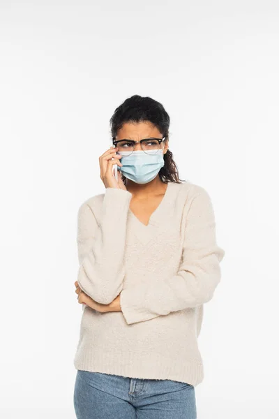 Triste femme afro-américaine en lunettes et masque médical parlant sur smartphone isolé sur blanc — Photo de stock
