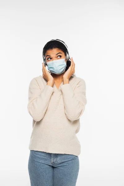 Africano americano mulher em máscara médica e fones de ouvido sem fio de pé isolado no branco — Fotografia de Stock