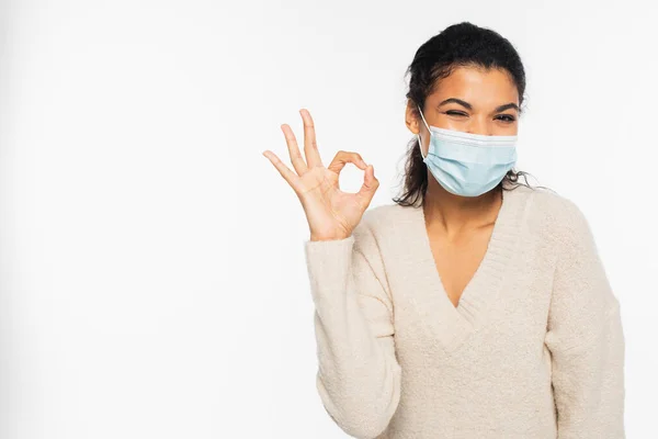 Afro-américaine femme en masque médical clin d'oeil et montrant ok signe isolé sur blanc — Photo de stock