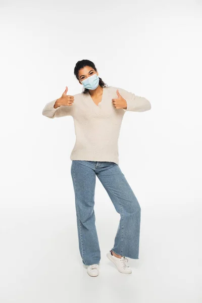 Full length of african american woman in medical mask showing thumbs up on white background — Stock Photo