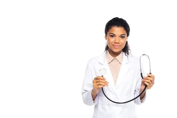 Young african american doctor in white coat holding stethoscope and looking at camera isolated on white — Stock Photo
