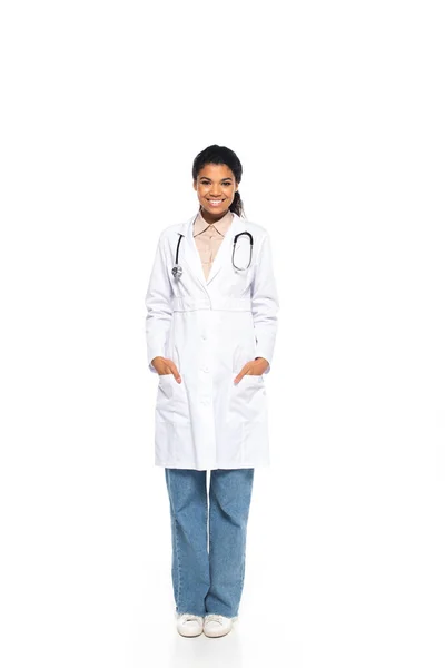 Полная длина улыбающийся африканский американский врач со стетоскопом глядя на камеру на белом фоне — стоковое фото