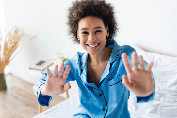 Happy african american woman in pajamas gesturing while sitting on bed — Stock Photo