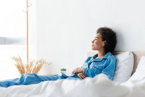 Happy african american woman in pajamas lying on bed — Stock Photo