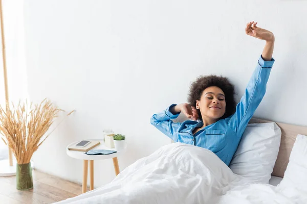 Erfreut afrikanisch-amerikanische Frau im Pyjama Stretching auf dem Bett — Stockfoto