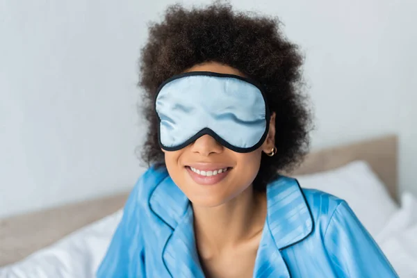 Femme afro-américaine gaie en pyjama bleu et masque de sommeil en soie — Photo de stock
