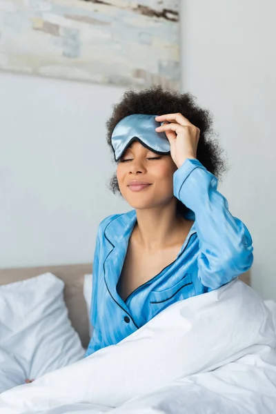 Smiling african american woman in pajamas adjusting sleeping mask — Stock Photo