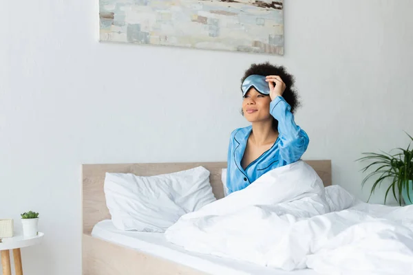 Sleepy african american woman in pajamas adjusting sleeping mask — Stock Photo