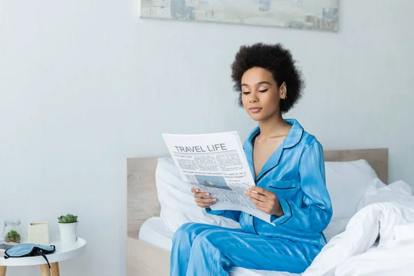 African american woman in pajamas reading travel life newspaper in bedroom — Stock Photo