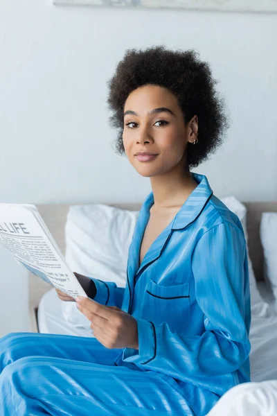 Afro-americana em pijama segurando viagem vida jornal no quarto — Fotografia de Stock