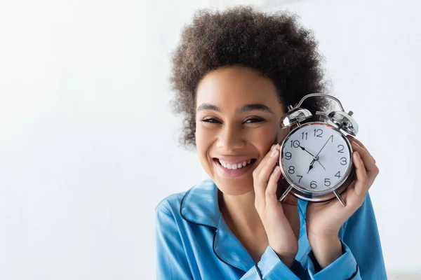 Mujer afro-americana positiva en pijama con despertador - foto de stock