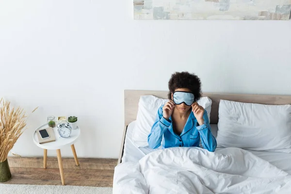 Vista de ángulo alto de la mujer afroamericana ajustando la máscara de dormir en el dormitorio - foto de stock