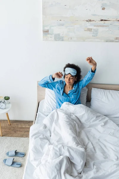 Blick aus der Vogelperspektive auf eine Afroamerikanerin mit Schlafmaske, die sich im Bett streckt — Stockfoto