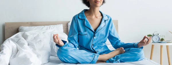 Vista recortada de mujer afroamericana en pijama meditando en la cama, pancarta - foto de stock