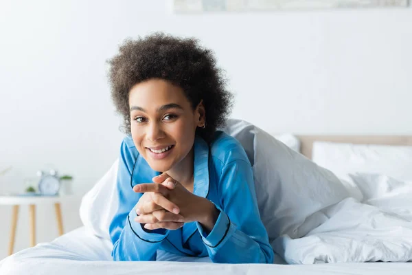 Happy african american woman in pajamas lying on bed — Stock Photo