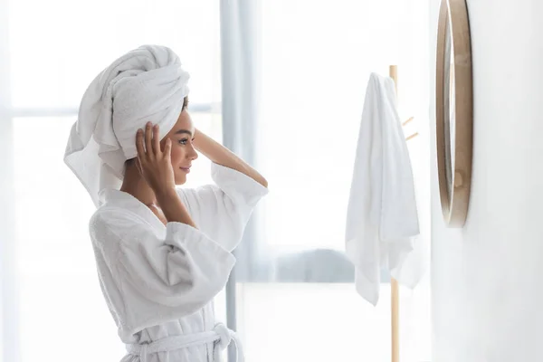 Joyful african american woman adjusting towel and looking at mirror in bathroom — Stock Photo