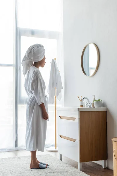 Young african american woman looking at mirror in bathroom — Stock Photo