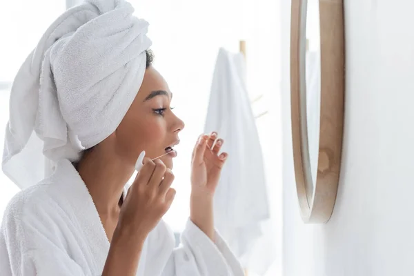 Vista lateral de la joven afroamericana en albornoz con hilo dental en el baño — Stock Photo