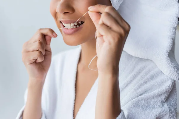 Cropped view of smiling young african american woman in bathrobe flossing teeth in bathroom — Stock Photo