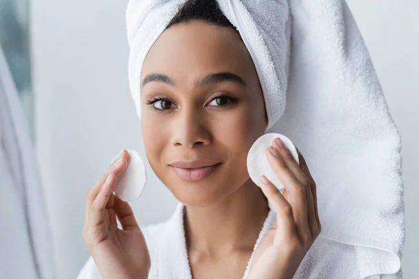 Femme afro-américaine souriante en serviette tenant des tampons de coton dans la salle de bain — Photo de stock