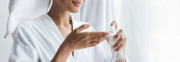 Vista recortada de la mujer afroamericana complacida sosteniendo botella con limpiador y almohadilla de algodón en el baño, pancarta - foto de stock