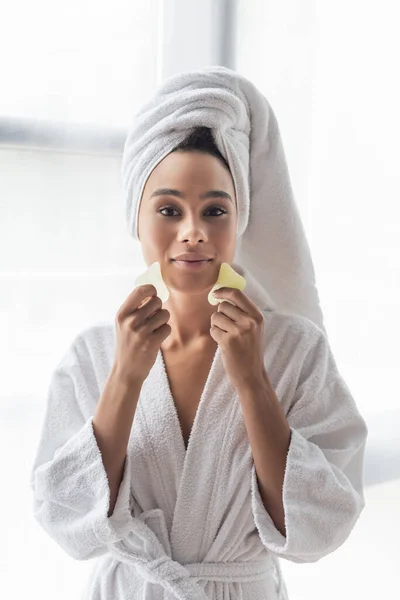 Giovane donna afroamericana in asciugamano bianco rottamazione viso con raschietti viso — Foto stock