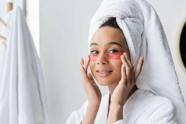 Happy african american woman applying eye patches in bathroom — Stock Photo