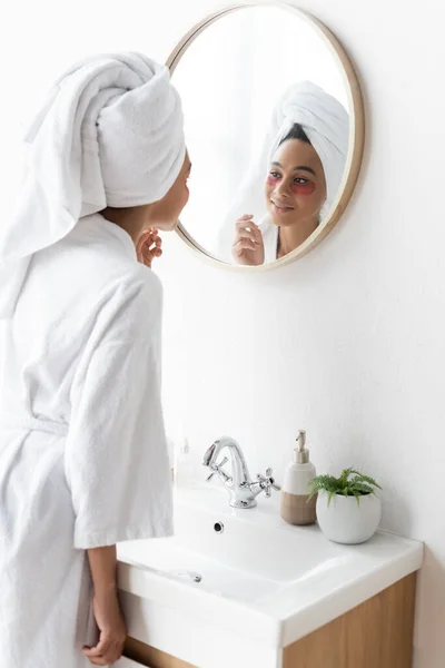 Alegre afroamericana mujer en parches de ojos mirando el espejo - foto de stock