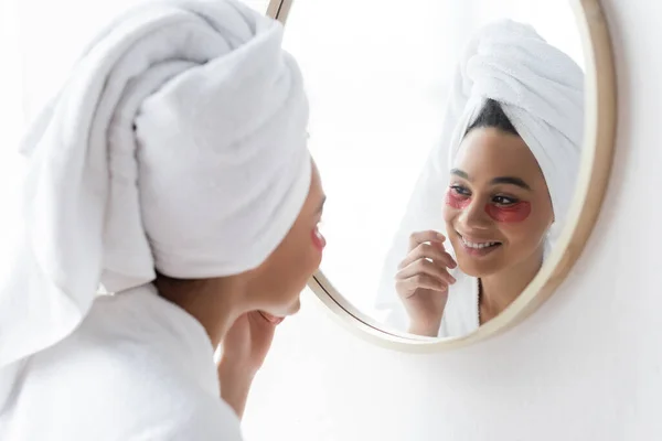 Happy african american woman in eye patches looking at mirror — Stock Photo