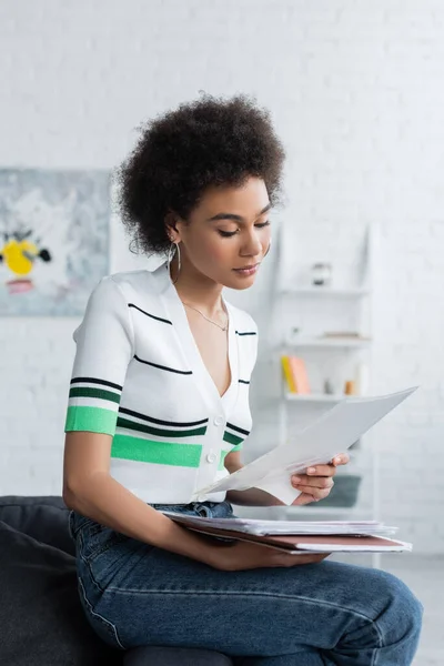 Lockige Afroamerikanerin schaut sich Dokumente im Wohnzimmer an — Stockfoto