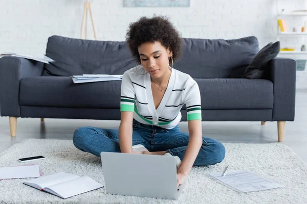 African american freelancer using laptop while sitting on carpet — Stock Photo