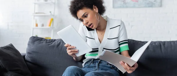 Beschäftigte afrikanisch-amerikanische Frau spricht auf Smartphone, während sie auf digitales Tablet schaut und Ordner, Banner in der Hand hält — Stockfoto