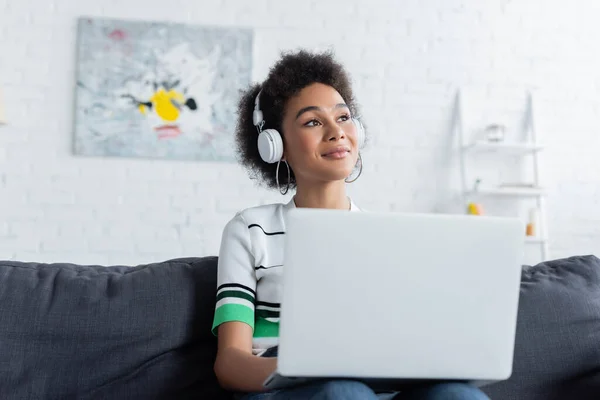 Pleased african american woman in wireless headphones using laptop — Stock Photo