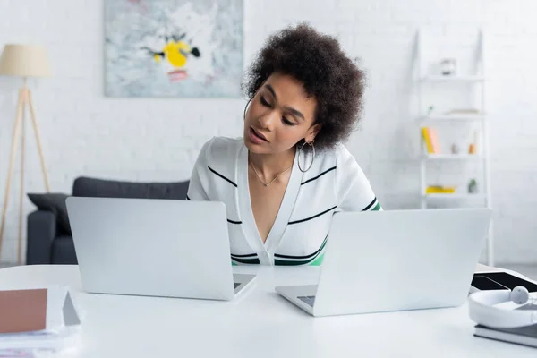 Freelancer afroamericano trabajando desde casa cerca de computadoras portátiles en el escritorio - foto de stock