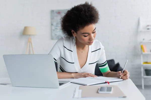 Mulher afro-americana escrevendo no notebook perto de gadgets — Fotografia de Stock